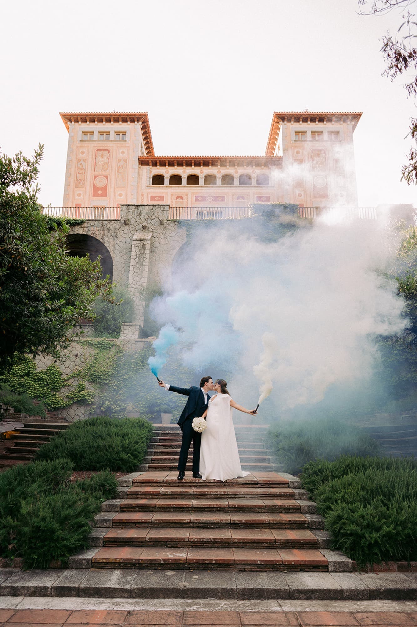 A couple on the steps of a palace surrounded by smoke flares