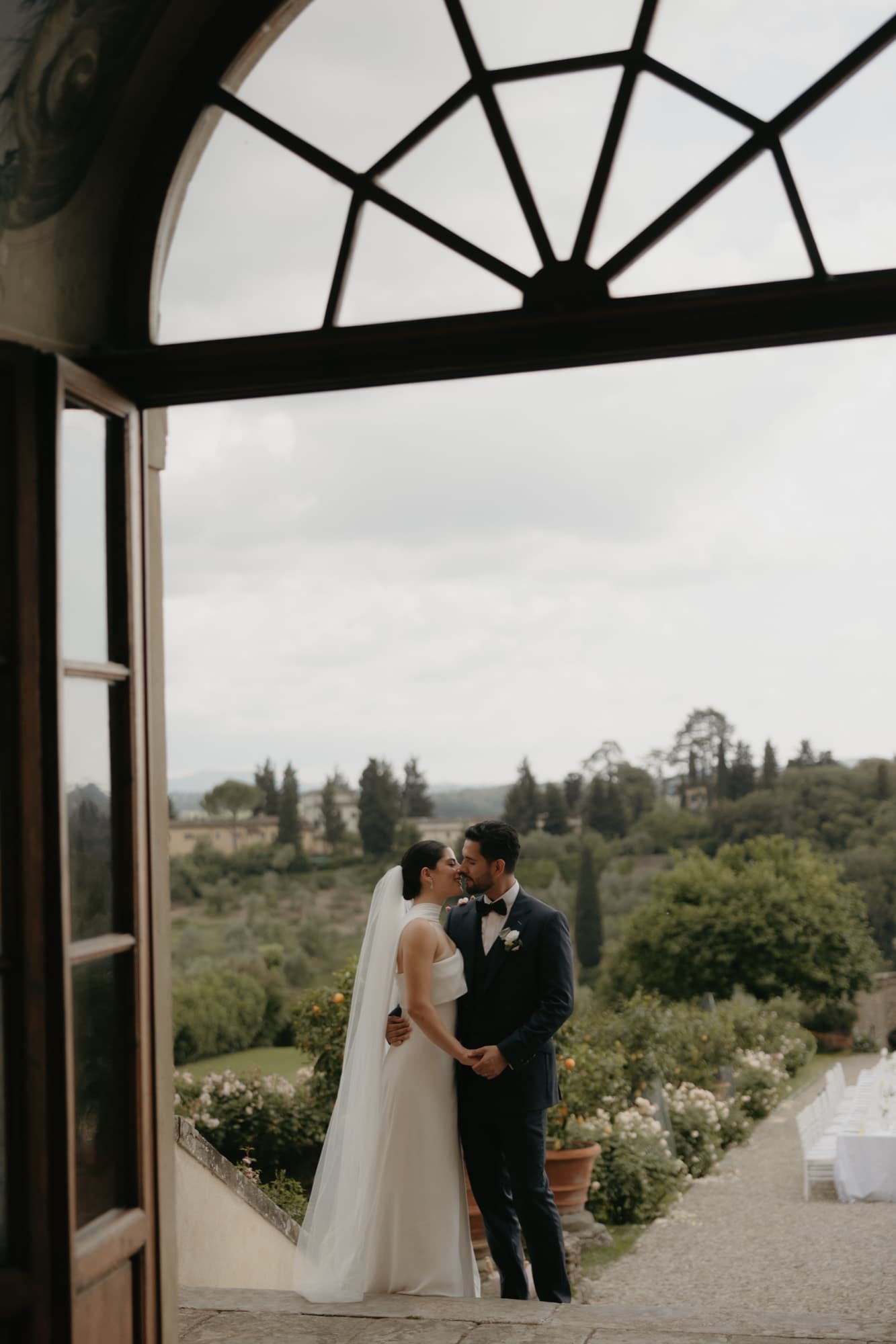 A couple leaning out of a tall window with the countryside behind